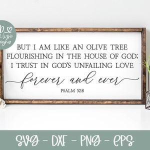 May include: A white wooden sign with a black inscription that reads "BUT I AM LIKE AN OLIVE TREE FLOURISHING IN THE HOUSE OF GOD; I TRUST IN GOD'S UNFAILING LOVE forever and ever PSALM 52:8". The sign is sitting on a white surface with a pink rose and a potted plant.