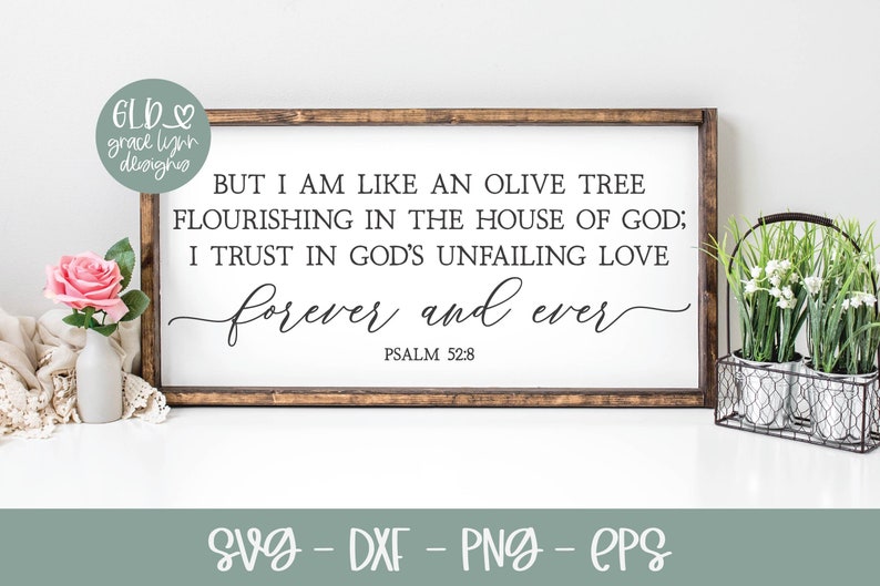 May include: A white wooden sign with a black inscription that reads "BUT I AM LIKE AN OLIVE TREE FLOURISHING IN THE HOUSE OF GOD; I TRUST IN GOD'S UNFAILING LOVE forever and ever PSALM 52:8". The sign is sitting on a white surface with a pink rose and a potted plant.