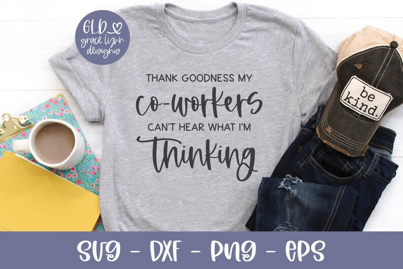 May include: A gray t-shirt with the text "THANK GOODNESS MY co-workers CAN'T HEAR WHAT I'M Thinking". The shirt is laying on a white surface with a pair of blue jeans and a brown baseball cap with the text "be kind." on it.