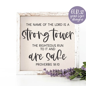 May include: A white wooden frame with a beige canvas insert. The canvas has black text that reads "The name of the Lord is a strong tower. The righteous run to it and are safe. Proverbs 18:10".