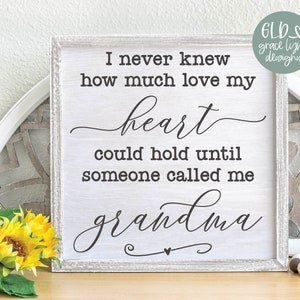 May include: A white sign with black text that reads "I never knew how much love my heart could hold until someone called me grandma". The sign is sitting on a table with sunflowers and a decorative wooden circle.