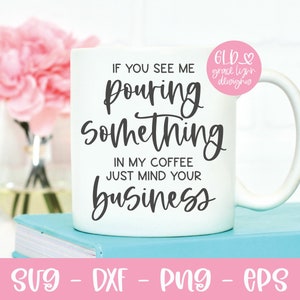 May include: White coffee mug with black text that reads "If you see me pouring something in my coffee just mind your business". The mug is sitting on a stack of blue books.