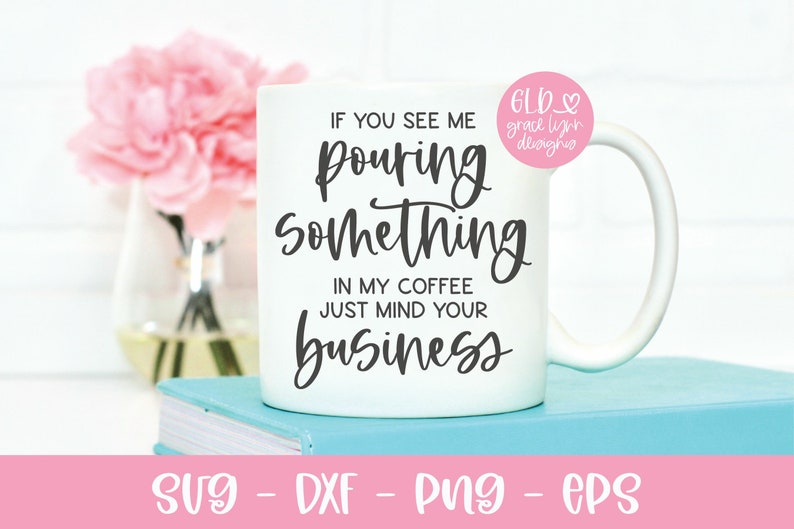 May include: White coffee mug with black text that reads "If you see me pouring something in my coffee just mind your business". The mug is sitting on a stack of blue books.