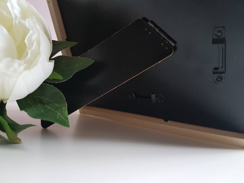 May include: A black picture frame with a wooden frame and a black easel stand. The frame is sitting on a white surface.
