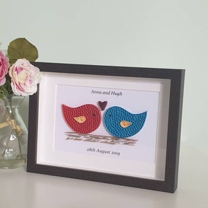May include: A framed paper craft artwork featuring two birds, one red and one blue, with a small heart above them. The text "Anna and Hugh" and "28th August 2019" is printed below the birds.