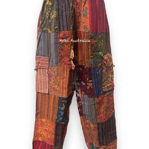 May include: Rust orange patchwork trousers with a drawstring waist. The trousers are made from a variety of fabrics and have a unique, bohemian style. "Achi Australia" is printed on the trousers.