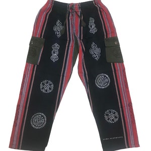 May include: Black and red striped pants with a green cargo pocket on each side. The pants have a drawstring waist and are decorated with white patterned circles.