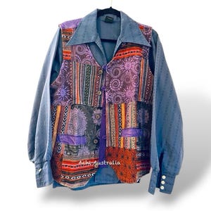 Könnte beinhalten: Ein blaues Langarmhemd mit einer mehrfarbigen Patchwork-Weste. Die Weste hat ein lila, rotes, orangefarbenes und schwarzes Muster. Das Hemd hat einen Knopfkrag und lange Ärmel. Die Weste hat einen Knopfverschluss.