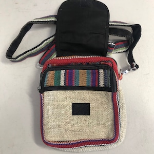 May include: A small, beige hemp crossbody bag with a black zipper and a colourful striped pattern around the edges. The bag has a black fabric pocket on the back.