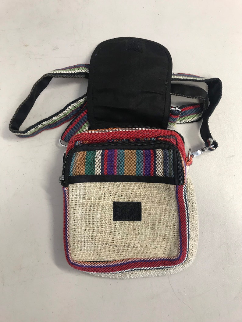 May include: A small, beige hemp crossbody bag with a black zipper and a colourful striped pattern around the edges. The bag has a black fabric pocket on the back.