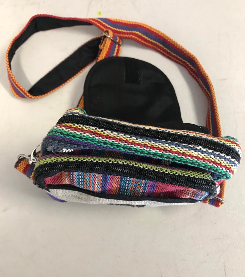 May include: A small, colourful, striped crossbody bag with a black zipper and a black strap. The bag has a small pocket on the back.