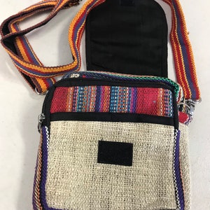 May include: A small, multi-coloured hemp bag with a zipper closure and a long adjustable strap. The bag has a woven design with a beige hemp fabric base and a colourful striped border. The strap is made of a woven fabric with red, orange, and blue stripes.