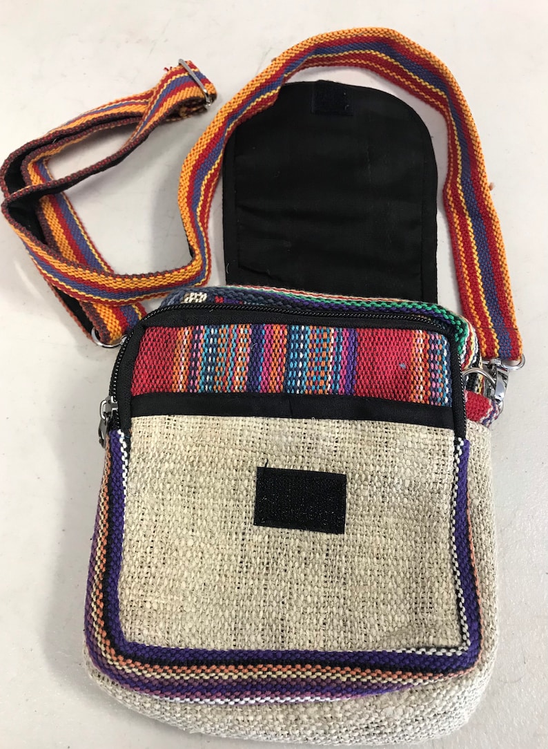 May include: A small, multi-coloured hemp bag with a zipper closure and a long adjustable strap. The bag has a woven design with a beige hemp fabric base and a colourful striped border. The strap is made of a woven fabric with red, orange, and blue stripes.