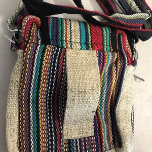 May include: A small, multi-coloured striped hemp bag with a long strap. The bag has a flap with a zipper closure and a small pocket on the front.