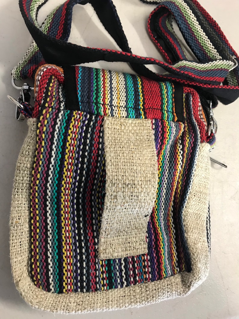 May include: A small, multi-coloured striped hemp bag with a long strap. The bag has a flap with a zipper closure and a small pocket on the front.