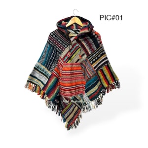 Może przedstawiać: Poncho z kapturem w stylu patchwork z różnorodnymi kolorowymi wzorami i fakturami. Poncho ma obszycie z frędzlami i jest prezentowane na drewnianym wieszaku. Tekst "PIC#01" jest widoczny w prawym górnym rogu.