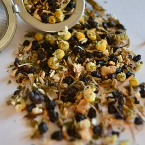 May include: A loose leaf tea blend with dried chamomile flowers, black tea leaves, and other herbs in a metal tea infuser.