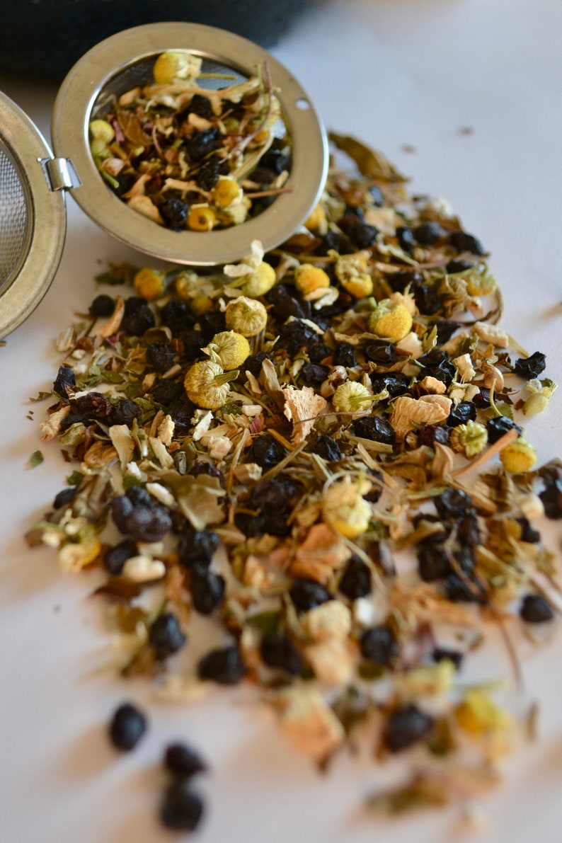 May include: A loose leaf tea blend with dried chamomile flowers, black tea leaves, and other herbs in a metal tea infuser.
