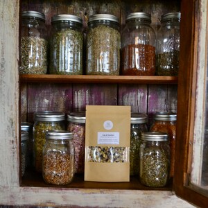 May include: A wooden cabinet with glass doors filled with glass jars containing dried herbs and spices. A brown paper bag with the text "Cup of Calm" is on the bottom shelf.
