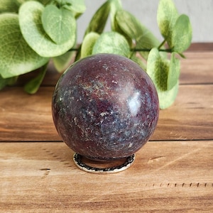 May include: A dark purple and blue gemstone sphere on a gold metal stand. The sphere is smooth and polished.