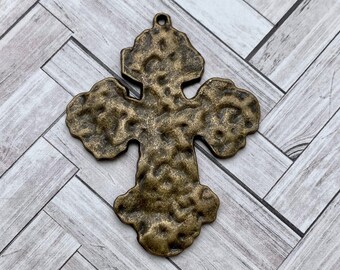 May include: A textured, antique gold-toned metal cross pendant. The cross has a hammered finish and a slightly distressed look.