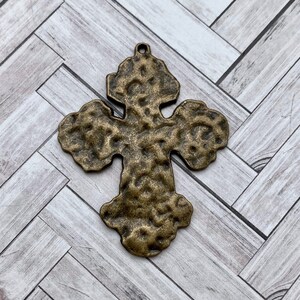 May include: A textured, antique gold-toned metal cross pendant. The cross has a hammered finish and a slightly distressed look.