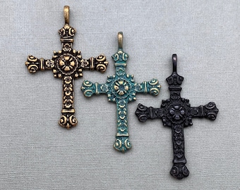 May include: Three ornate metal crosses with different finishes: gold, teal, and black. Each cross has a detailed design with a floral pattern.