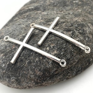 May include: Two silver metal cross charms with jump rings. The crosses are simple and elegant, perfect for adding a touch of faith to jewelry projects.