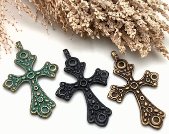 May include: Three ornate metal cross pendants in different colors: green, black, and gold. Each cross has a detailed design with circles and swirls.