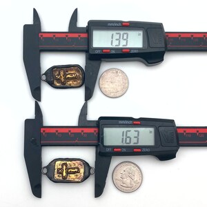 May include: Two gold cross pendants measured with calipers. The top pendant measures 1.39 inches and the bottom pendant measures 1.63 inches.
