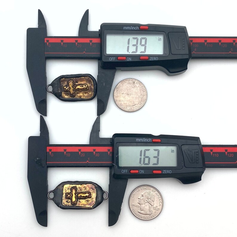 May include: Two gold cross pendants measured with calipers. The top pendant measures 1.39 inches and the bottom pendant measures 1.63 inches.