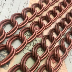 May include: Close-up of a copper chain with oval links. The chain is made of two strands of wire twisted together to form the links.