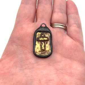 May include: A small, black pendant with a gold cross design. The cross is detailed with a textured pattern.