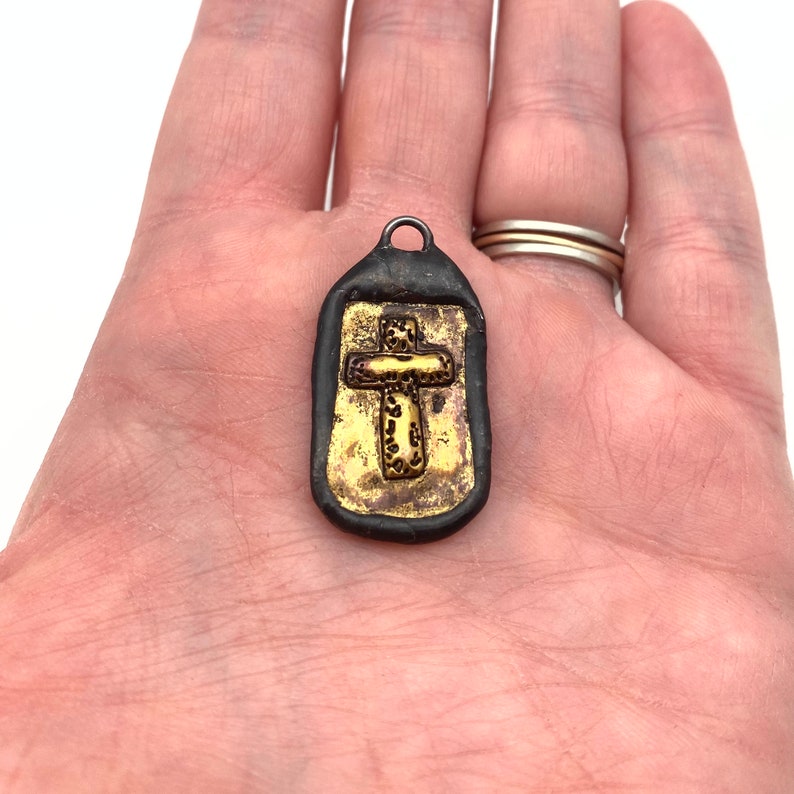 May include: A small, black pendant with a gold cross design. The cross is detailed with a textured pattern.