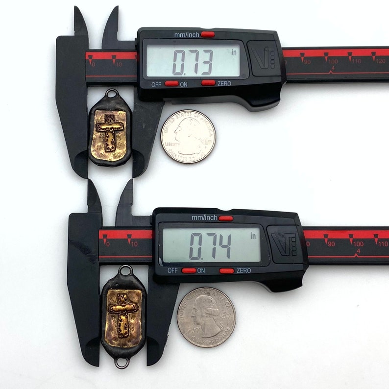 May include: Two gold-toned metal cross charms with a textured surface, measured with a digital caliper. The charms are approximately 0.73 inches and 0.74 inches in size.