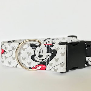 K&ouml;nnte beinhalten: Wei&szlig;er Hundehalsband mit einer schwarzen Schnalle und einem silbernen Ring. Das Halsband hat ein sich wiederholendes Muster aus Mickey Mouse-K&ouml;pfen in Schwarzwei&szlig; mit roten Akzenten.