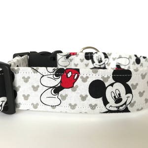 K&ouml;nnte beinhalten: Wei&szlig;er Hundehalsband mit einem schwarzen und roten Mickey Mouse-Druck. Das Halsband hat eine schwarze Schnalle und einen silbernen D-Ring.
