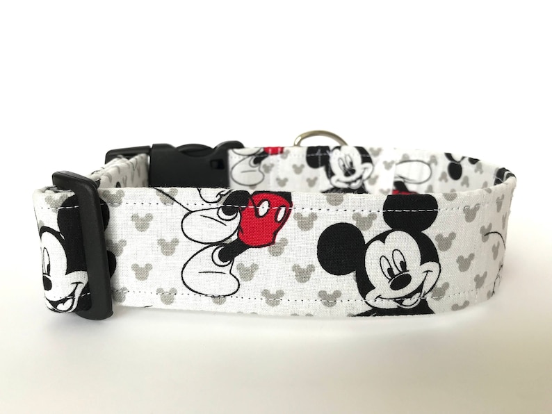K&ouml;nnte beinhalten: Wei&szlig;er Hundehalsband mit einem schwarzen und roten Mickey Mouse-Druck. Das Halsband hat eine schwarze Schnalle und einen silbernen D-Ring.