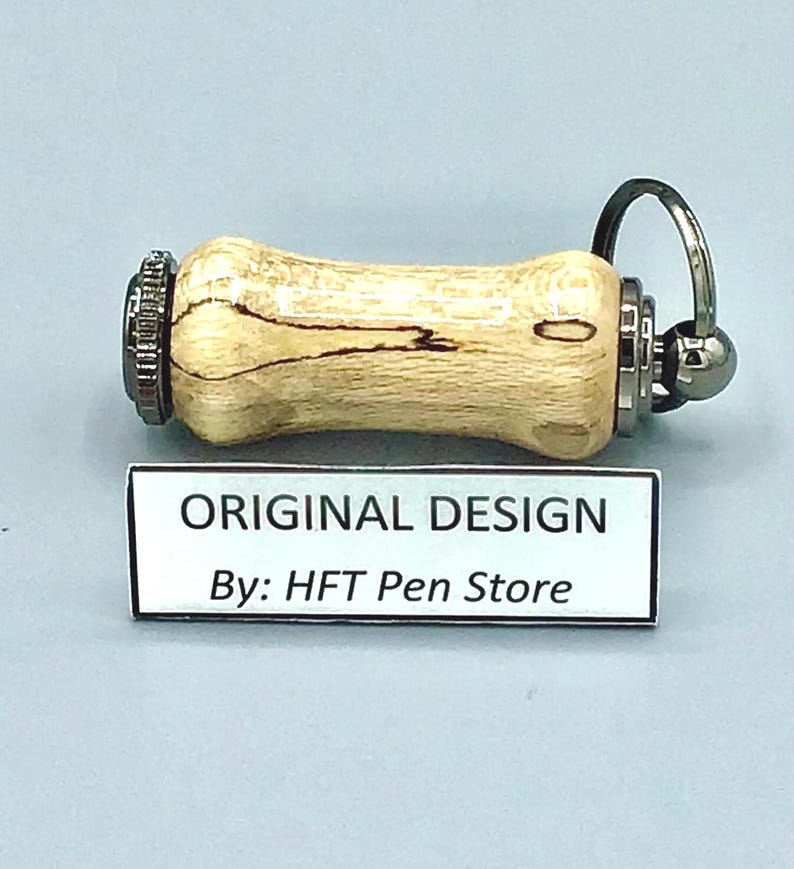 Pode incluir: Uma caneta artesanal com um corpo de madeira clara e padr&otilde;es de gr&atilde;o escuros. Possui detalhes em metal e um porta-chaves. O texto "ORIGINAL DESIGN By: HFT Pen Store" est&aacute; em uma etiqueta branca.