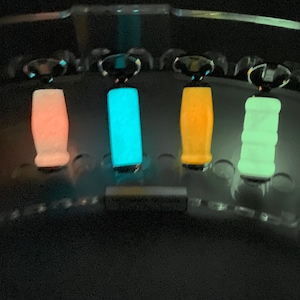 May include: Four glow-in-the-dark bottle stoppers in different colors: pink, blue, yellow, and green. The stoppers are displayed in a clear plastic holder.
