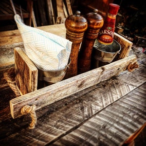 May include: A rustic wooden serving tray with rope handles, featuring two wooden salt and pepper shakers, a small metal container with a white napkin, and a bottle of malt vinegar.