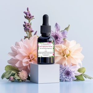 May include: A dark glass bottle of anti-aging face serum with a black dropper, set on a white cube. The label reads "Anti-Aging Face Serum Skin Smoothing & Brightening." The bottle is surrounded by pink, peach, and purple flowers.