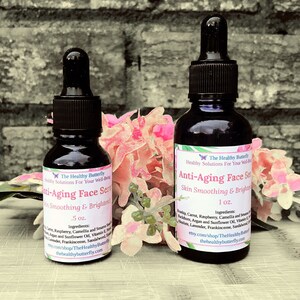 May include: Two dark glass bottles of Anti-Aging Face Serum with black droppers. The bottles are labeled with white text, including the brand name "The Healthy Butterfly" and the serum's purpose. The bottles are .5 oz and 1 oz. Pink flowers are in the background.