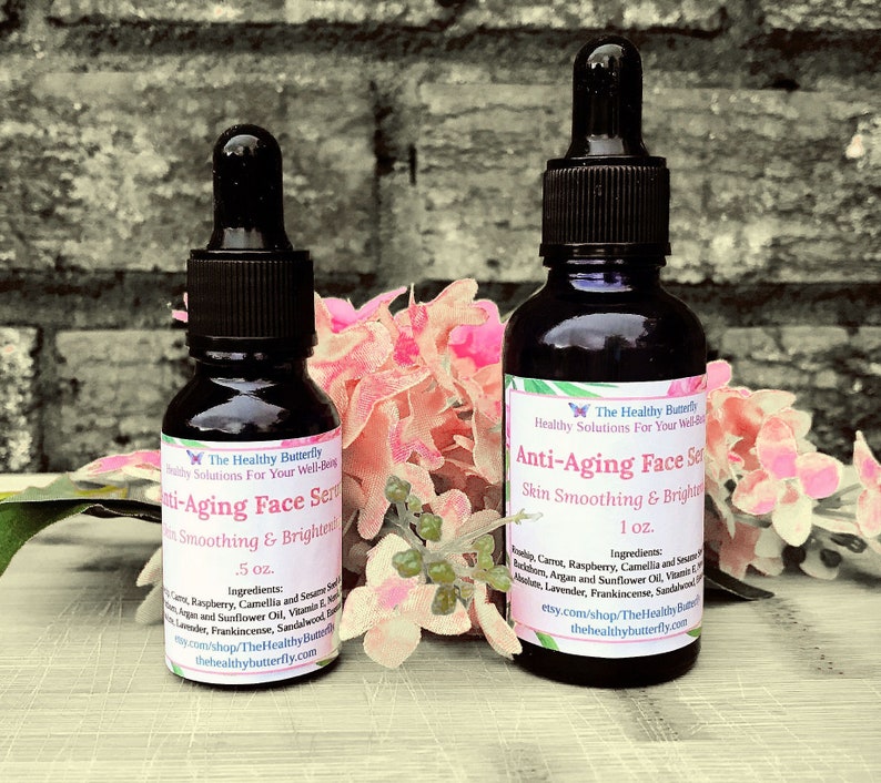 May include: Two dark glass bottles of Anti-Aging Face Serum with black droppers. The bottles are labeled with white text, including the brand name "The Healthy Butterfly" and the serum's purpose. The bottles are .5 oz and 1 oz. Pink flowers are in the background.