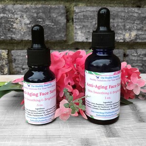 May include: Two dark blue glass bottles of anti-aging face serum with black droppers. The bottles are labeled with white text, including the brand name "The Healthy Butterfly" and the serum's purpose: "Skin Smoothing & Brightening."
