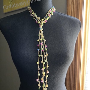May include: A multi-strand necklace with colorful beads in shades of pink, yellow, green, and blue. The necklace is displayed on a black mannequin. The text "Creatively Damaris" is visible in the background.