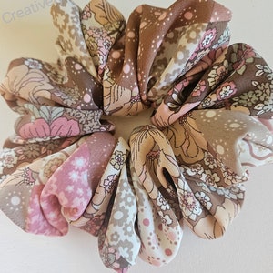 May include: A brown, pink, and white floral patterned scrunchie. The scrunchie is made of fabric and is tied in a knot.