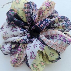 May include: A colorful patterned fabric hair scrunchie in shades of yellow, white, pink, and black. The scrunchie is made of a soft, silky fabric and is perfect for holding hair in place.