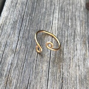 May include: A gold-toned ring with a unique, twisted design. The ring has two small circles on the band.