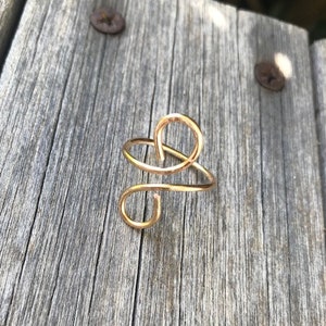 May include: A gold-toned wire ring with a unique, abstract design. The ring is made of a single piece of wire that is twisted and shaped into a spiral.